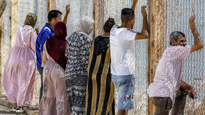 Relatives and friends wait by a fence topped with barbed-wire the Spanish enclave of Ceuta, at the Bab Ceuta border post near the town of Fnideq in Morocco on 2 August, 2026.