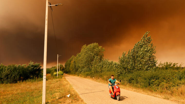 A man rides a scooter beneath a smoke-filled sky as a wildfire burns in Deliblatska Pescara, some 70 kilometres northeast of Belgrade, Serbia, on August 20, 2026