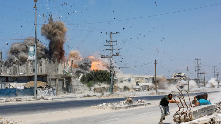 People run for cover, as debris flies through the air, during an Israeli strike, carried out after the Israeli military warned residents to evacuate the area, Al-Zawayda, in the central Gaza Strip