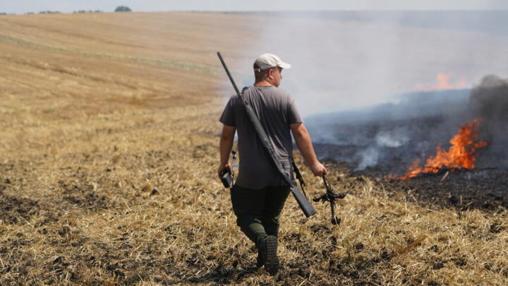A farmer carries a part of a Russian FPV drone that he shot down with a rifle as he watches a field burn following an air attack in the Kharkiv region, Ukraine, Wednesday, August 5, 2026
