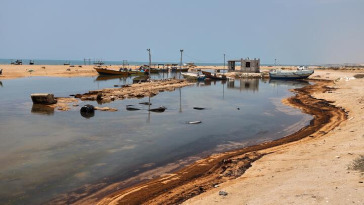 Oil residue lines the shore near fishing boats on Iran's Qeshm Island in the Strait of Hormuz on August 13, 2026.