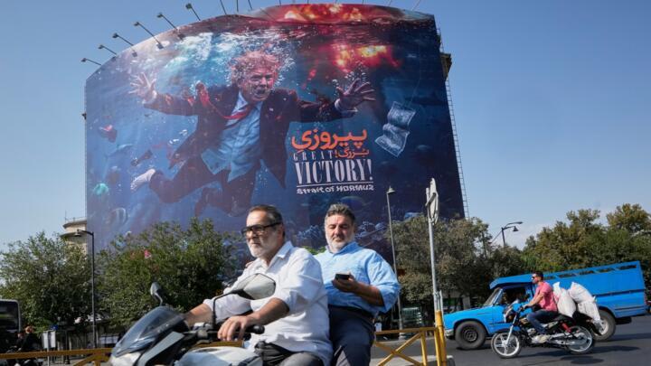 Motorcyclists in Tehran pass a billboard depicting President Donald Trump underwater amid explosions with the words "Great Victory! Strait of Hormuz," on August 24, 2026