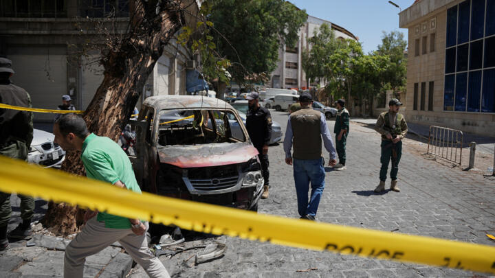 Syrian security personnel inspect a burned vehicle after two explosions rocked the area earlier while Syrian President Ahmad al-Sharaa met French President Emmanuel Macron.