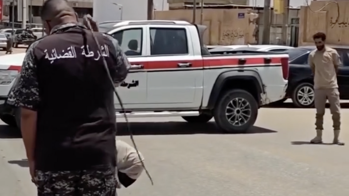 July 21st 2026, Sabha, Libya: a woman is sentenced to 100 lashes for adultery. She is seen kneeling on a mattress in the middle of a street blocked by a judicial police vehicle. One officer reads out the verdict, then another carries out the sentence. © Instagram / @feminists_of_libya